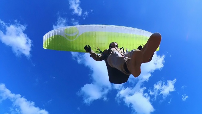 青空を背景に、頭上をフライトするパラグライダー